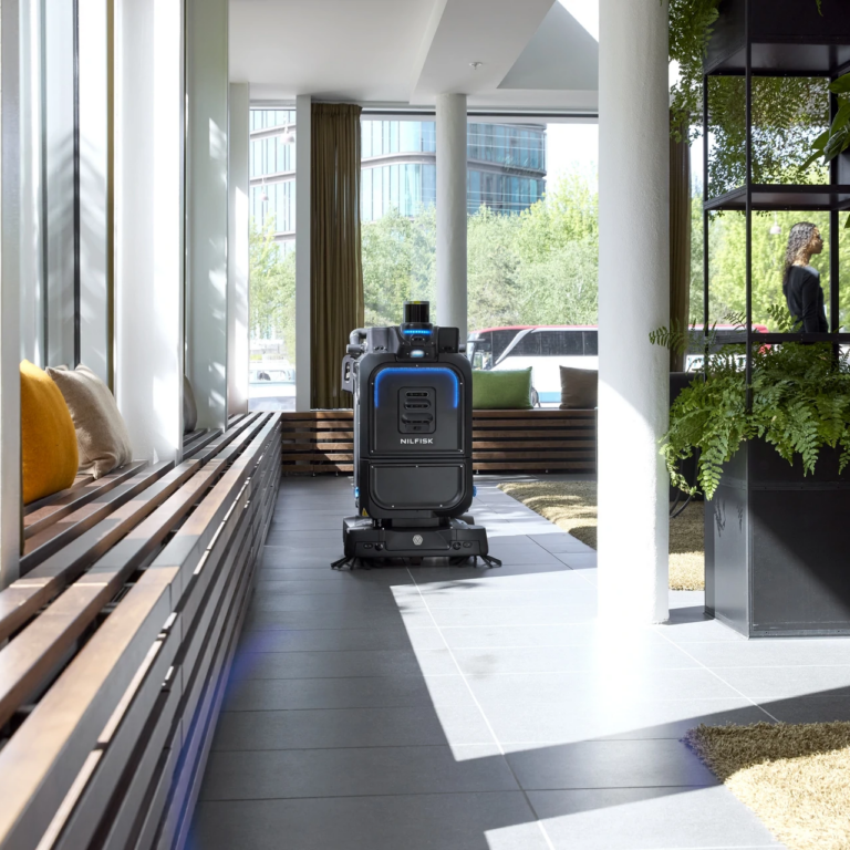 Nilfisk autonomous floor scrubber cleaning a tiled lobby beside lounge seating